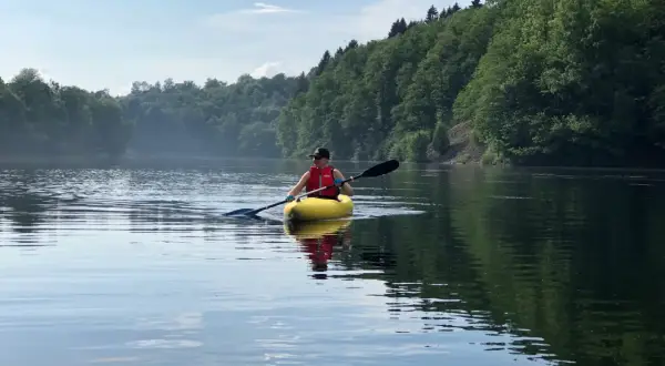 Person in gelbem Kajak genießt eine friedliche Kanu fahrt auf einem ruhigen See, umgeben von üppigen grünen Wäldern.