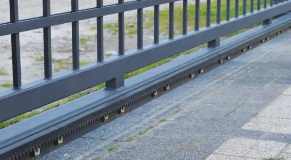 Metalowa listwa zębata do bramy przesuwnej, z widocznymi ząbkami i rolkami prowadzącymi.