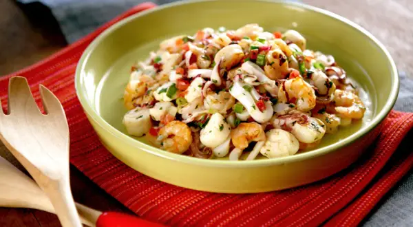 Deliciosa ensalada de marisco con camarones, calamares y vieiras, aderezada con hierbas frescas y pimientos.