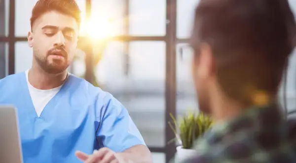 Lekarz w niebieskiej koszuli rozmawia z pacjentem. Czy trzeba mieć skierowanie do psychiatry? Zapytaj lekarza.