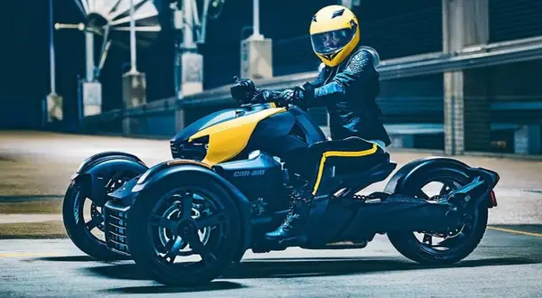 Kierowca w żółtym kasku na futurystycznym motorze trójkołowym Can-Am, gotowy do jazdy.