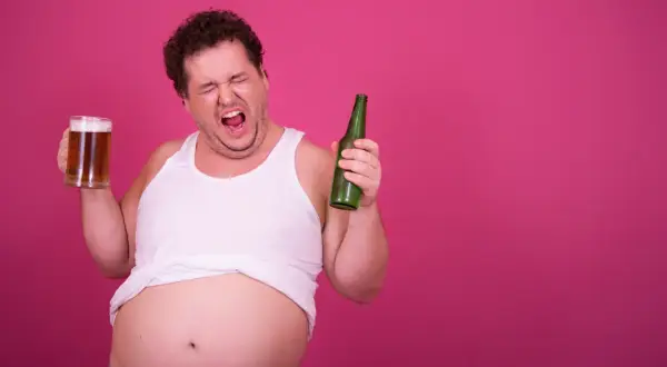 Mężczyzna z piwnym brzuchem krzyczy, trzymając kufel piwa i butelkę, zastanawiając się, czy wódka tuczy.