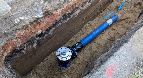 Blaues Rohr mit Ventil in einem ausgehobenen Graben.
