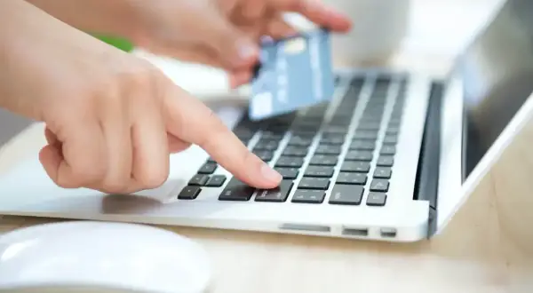 Dłoń z kartą zbliża się do klawiatury laptopa, gotowa do płatności. To jak szybkie przelewy przez Skrill, wygodne i bezpieczne.