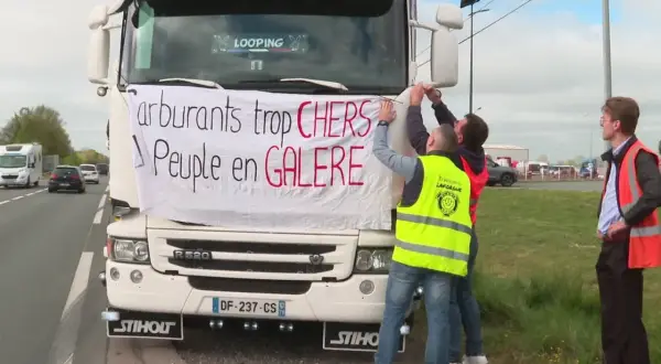 Des routiers accrochent une banderole sur un camion : "Carburants trop CHERS, Peuple en GALERE". Ils expriment leur mécontentement face au prix du carburant.