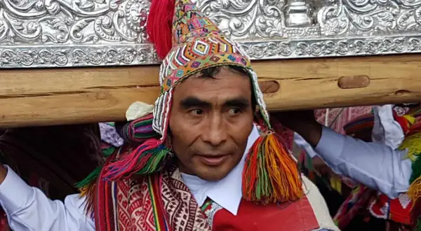 Kolorowy strój i tradycyjna czapka zdobią jednego z mężczyzn niosących ozdobną ramę. To **Indianie z Cuzco** podczas uroczystości.