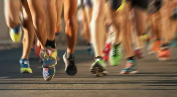 Nogi biegaczy w ruchu, niektórym po bieganiu grozi biegunka. Kolorowe buty sportowe na asfalcie.