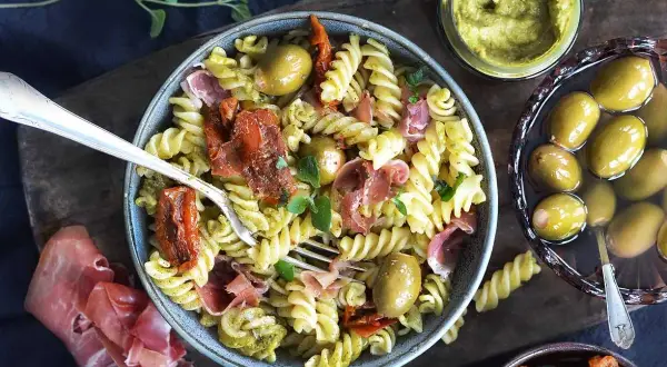 Pasta salad with pesto, sun-dried tomatoes, olives, and prosciutto.