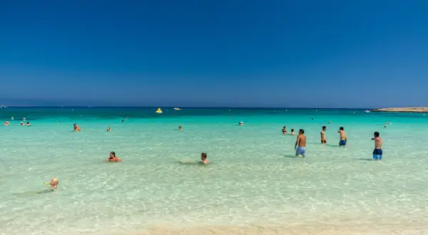 Ludzie kąpią się w krystalicznie czystej wodzie na plaży Makronissos. Słońce świeci, a niebo jest bezchmurne.