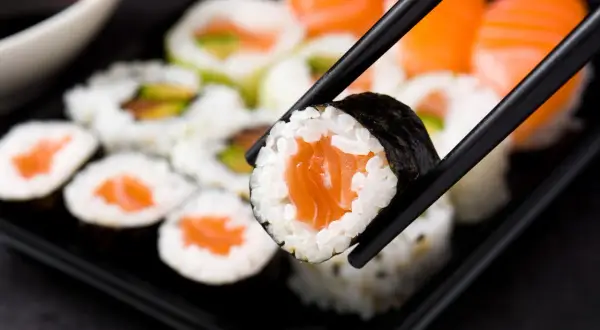 Chopsticks podnoszą kawałek sushi z łososiem. Czy sushi jest zdrowe? Tak, jeśli jest przygotowane z ryżu, ryb i warzyw.
