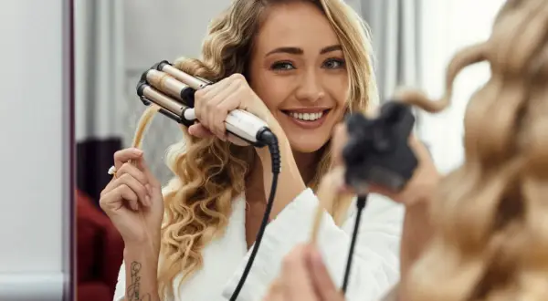 Uśmiechnięta blondynka tworzy sobie fale hollywoodzkie za pomocą lokówki.