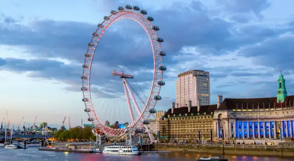 London Eye oświetlone wieczorem, z widokiem na Tamizę i budynki w tle.