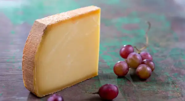 Un morceau de Comté aux cristaux savoureux, accompagné de grappes de raisins rouges sur un fond texturé.