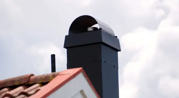 Schwarzer Schornstein mit Haube, Dachziegel und ein kleines schwarzes Rohr. Beachten Sie die schornstein revisionsklappe vorschriften.