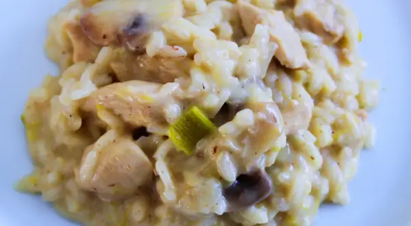 Un crémeux risotto poulet aux champignons et poireaux, servi sur une assiette blanche. Un plat réconfortant et savoureux.