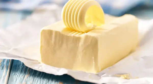 Un rouleau de beurre jaune, frais et crémeux, est posé sur un bloc de beurre, prêt à être tartiné.
