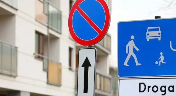 Znak b35 zakazu zatrzymywania się i postoju, obok znak drogi dla pieszych i rowerzystów, na tle nowoczesnego budynku.