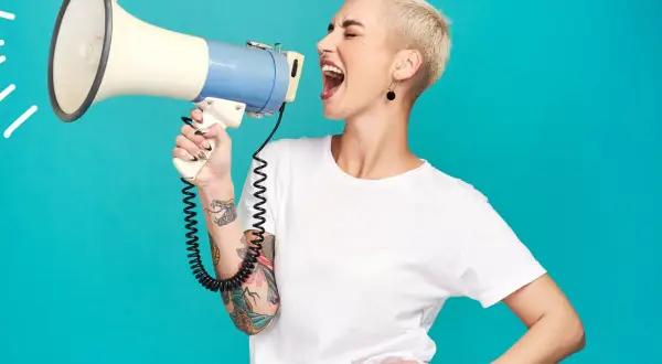 Mujer con pelo corto y tatuajes grita por un megáfono, mostrando el poder femenino.