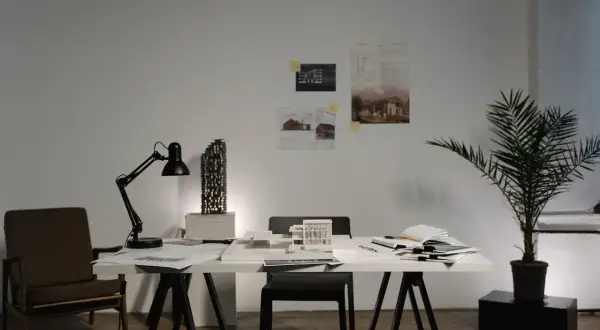 Biuro architektoniczne z modelem budynku, lampą, krzesłem i dokumentacją. Karta nadzoru autorskiego czeka na zatwierdzenie.