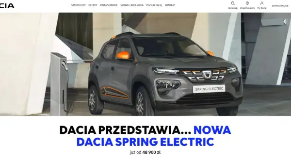 Szara dacia elektryczna Spring Electric z pomarańczowymi akcentami ładuje się przy stacji.