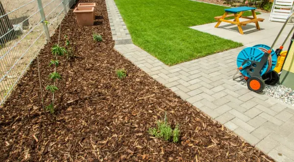 Gepflegter Garten mit frisch gemulchtem Beet, das trotz vereinzelten Unkräutern gut aussieht. Rasen mulchen ist hier die Devise.