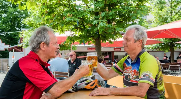 Zwei Radfahrer stoßen im Stadtbiergarten Schorndorf mit Bier an.