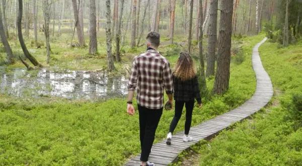 Para spaceruje drewnianą kładką przez las w kierunku jeziora kacze oko.