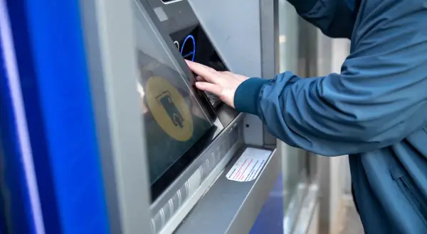 Osoba w granatowej kurtce korzysta z bankomatu, by dokonać żabka wypłata gotówki.