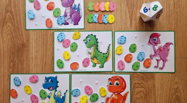 Zabawa edukacyjna na dzień dinozaura w przedszkolu: kolorowe jajka do przyklejania na planszach z dinozaurami.
