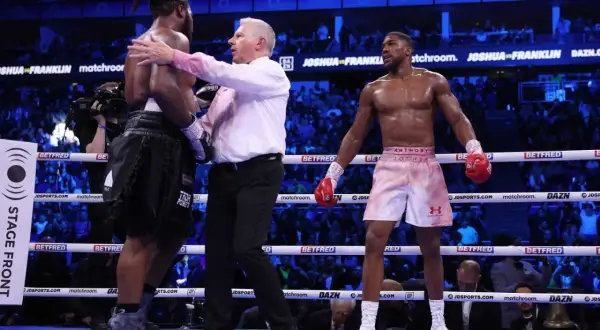 Referee separates two boxers, Anthony Joshua and Dillian Whyte, in a boxing ring. The boxing scoring system is in effect as judges tally the rounds.