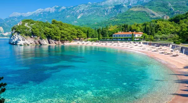 Krystalicznie czysta woda i piaszczysta plaża z leżakami, otoczone zielenią i górami. To jedna z najpiękniejszych plaż Czarnogóry.