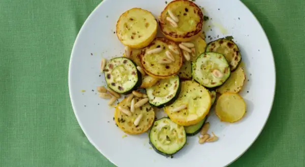 Zucchini gebraten italienisch mit Pinienkernen auf einem weißen Teller. Ein köstliches Gericht, das an einen sonnigen Tag in Italien erinnert.