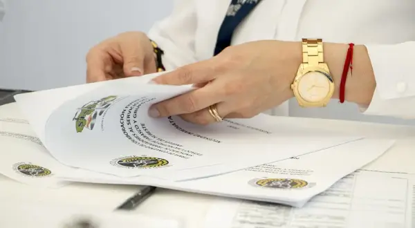 Dłonie przeglądają dokumenty, wśród których znajdują się oświadczenia o poddaniu się egzekucji. Złoty zegarek i czerwona nitka na nadgarstku.