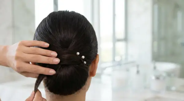 En person stylar en elegant chinjong frisyr med pärlklädda hårnålar.