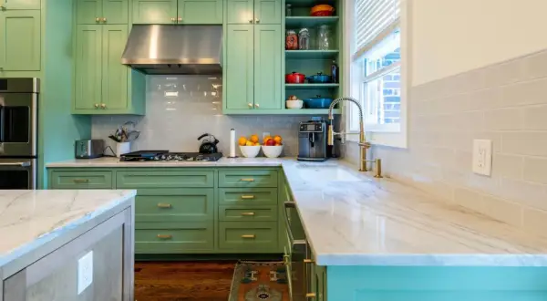 Elegante cocina verde agua y madera con encimeras de mármol, electrodomésticos de acero inoxidable y detalles dorados.