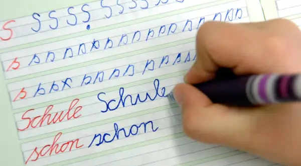 Kind übt das **Buchstaben schreiben lernen** auf liniiertem Papier. Es schreibt die Buchstaben S, b, p und die Wörter "Schule" und "schon".