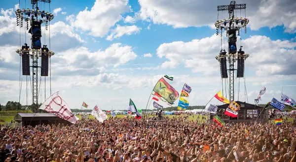 Tłum ludzi na festiwalu pod sceną z wieżami nagłośnieniowymi i flagami.