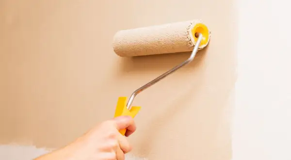 Mano che usa un rullo per pitturare una parete di color sabbia. Impara come pitturare con il rullo per un risultato perfetto.