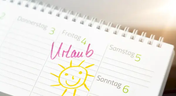 Kalendarz z zaznaczonym "Urlaub" (urlop) i uśmiechniętym słońcem. Dzień wolny w Niemczech, czas na odpoczynek!