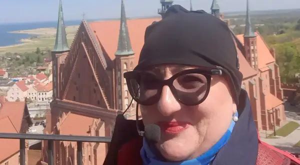 Kobieta w okularach i czapce na tle Fromborka. Wspaniałe widoki, idealne na rodzinne wycieczki i atrakcje dla dzieci.