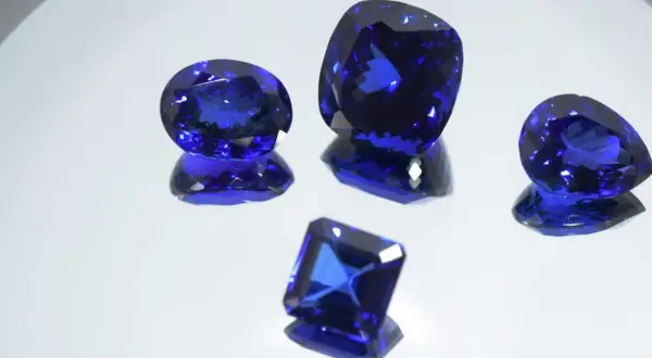 Cinco gemas de tanzanita piedra, de cortes y tamaños variados, brillan con un intenso color azul sobre un fondo reflectante.