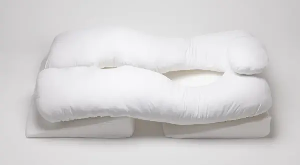 A white, U-shaped body pillow, designed for comfort and support, rests on wedge-shaped cushions. These almohadas ortopédicas offer a cozy embrace.