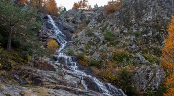 Cascada de Mojonavalle en otoño, con rocas cubiertas de musgo y árboles de hojas doradas.
