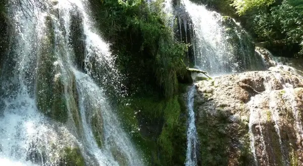 Cascada exuberante, ideal para saber qué visitar en Bulgaria. El agua cae sobre rocas cubiertas de musgo y vegetación frondosa.