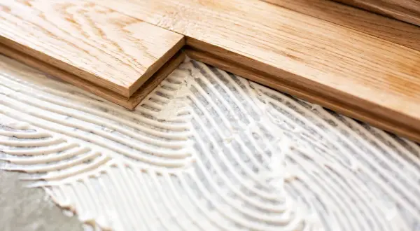 Pose de parquet en bois sur du béton avec de la colle. Les lames de bois sont prêtes à être fixées.