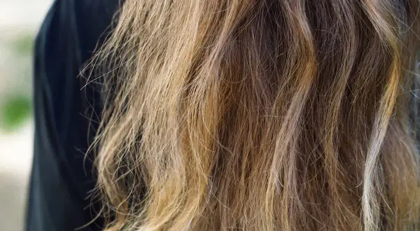 Chevelure châtain aux reflets blonds, légèrement ondulée, montrant l'effet de l'eau sur les cheveux.