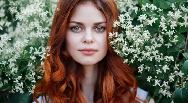 Eine Frau mit leuchtend roten, bunten Haaren blickt aus einem Meer von weißen Blüten.