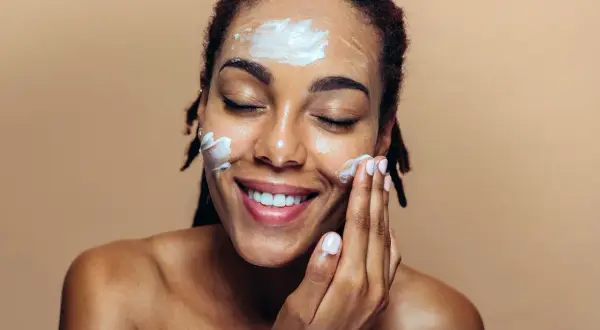 Une femme applique une crème hydratante sur son visage, un geste essentiel pour un maquillage jour parfait.