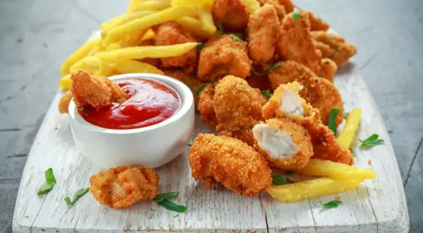 Chrupiące nuggetsy w płatkach kukurydzianych, podane z frytkami i ketchupem. Idealna przekąska na każdą okazję.