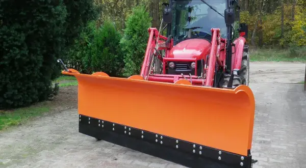 Czerwony traktor z zamontowanym pomarańczowym pługiem do orania, gotowy do pracy na jesiennej drodze.
